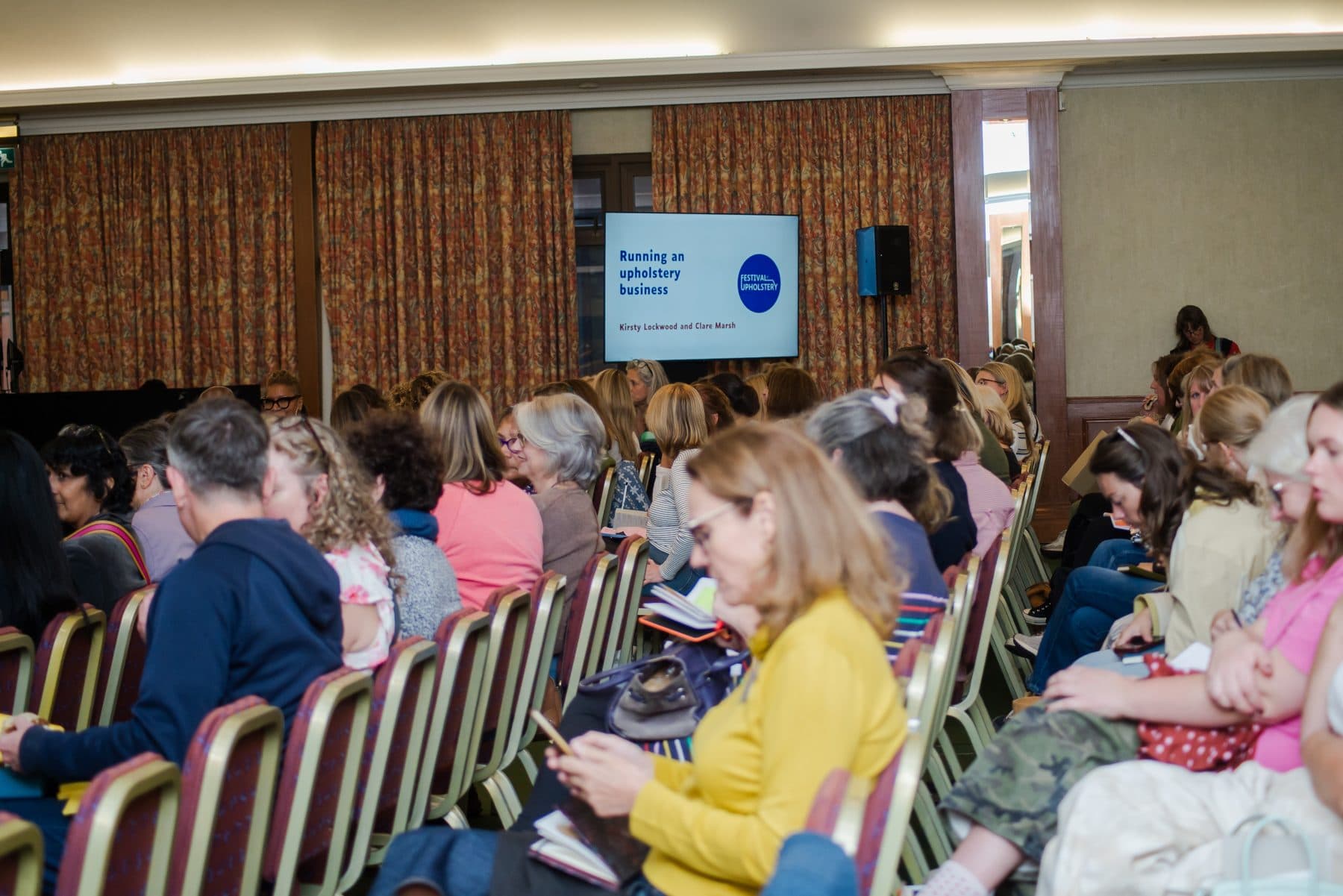 The audience at the Festival of Upholstery 2026 watching a presentation relayed to the big screen