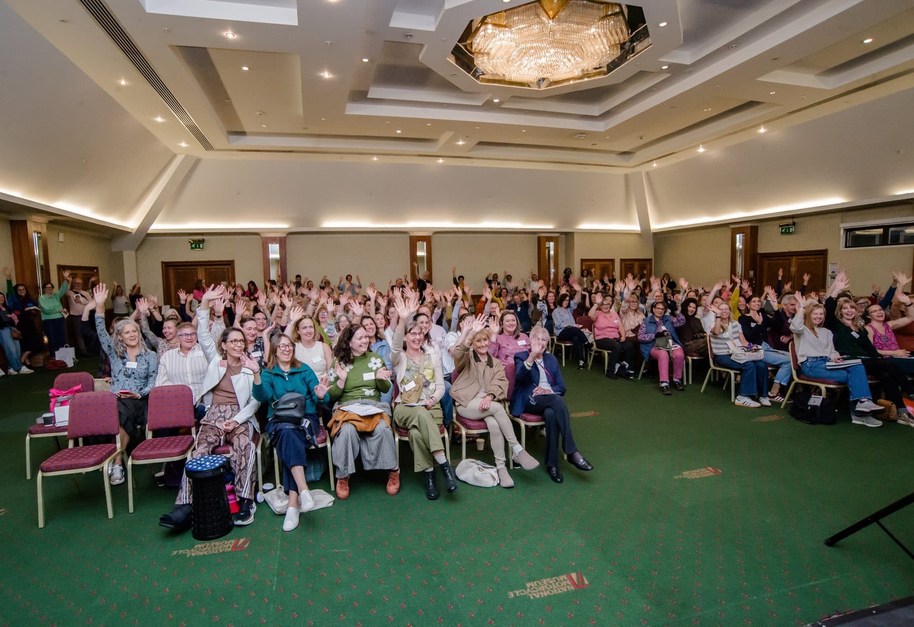 The main room at the Festival of Upholstery 2026, National Conference Centre, Solihull, with the audience's hands raised