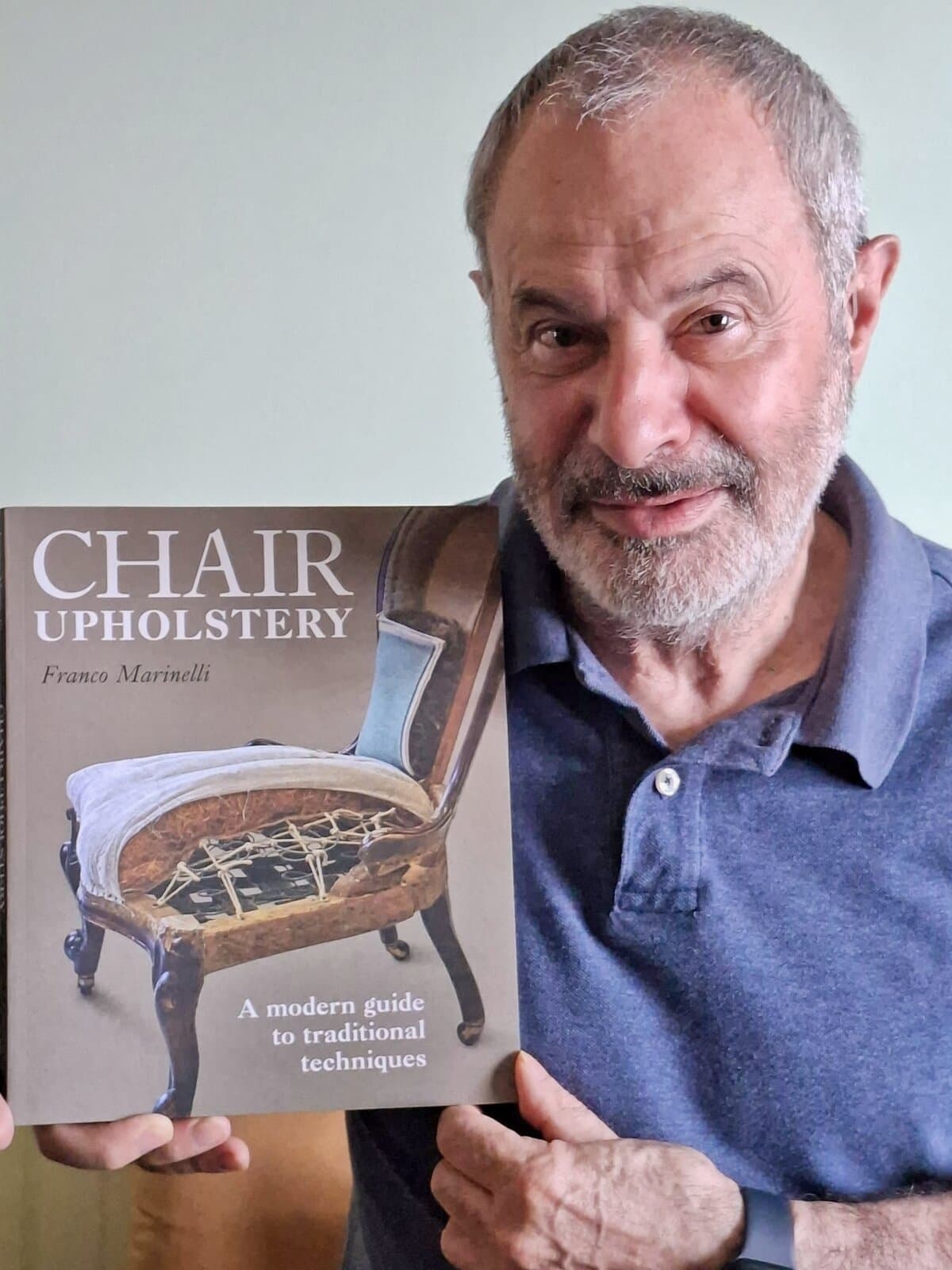 Franco Marinelli holding a copy of his book Chair Upholstery