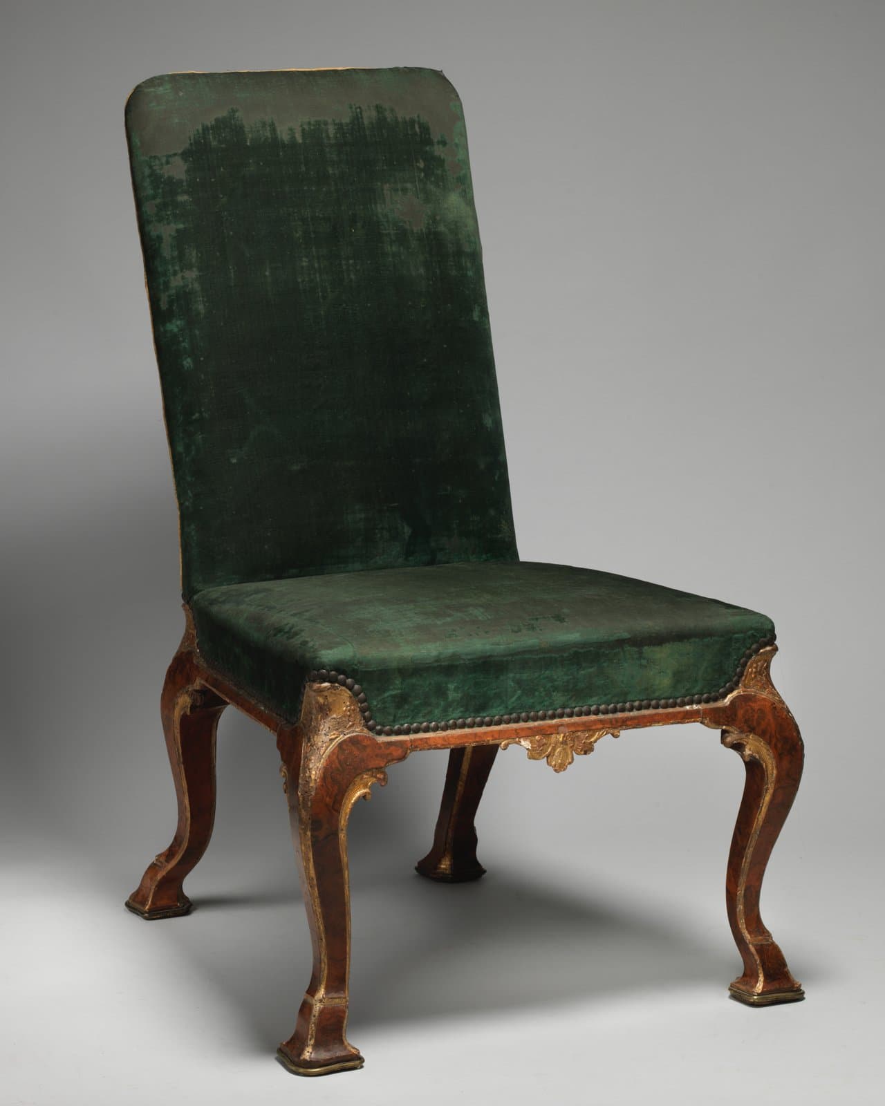 Side chair of about 1715 with a tall upholstered back and seat in worn green velvet, close-nailed seat rail and walnut cabriole legs with gilt carving