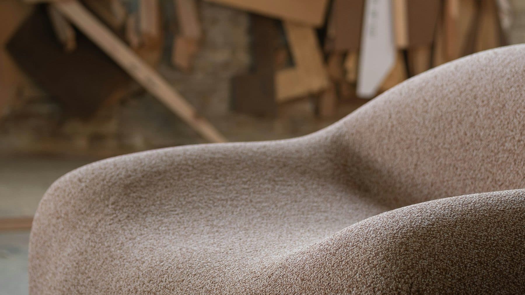 A curved upholstered piece in a workshop, with paper patterns hanging behind it