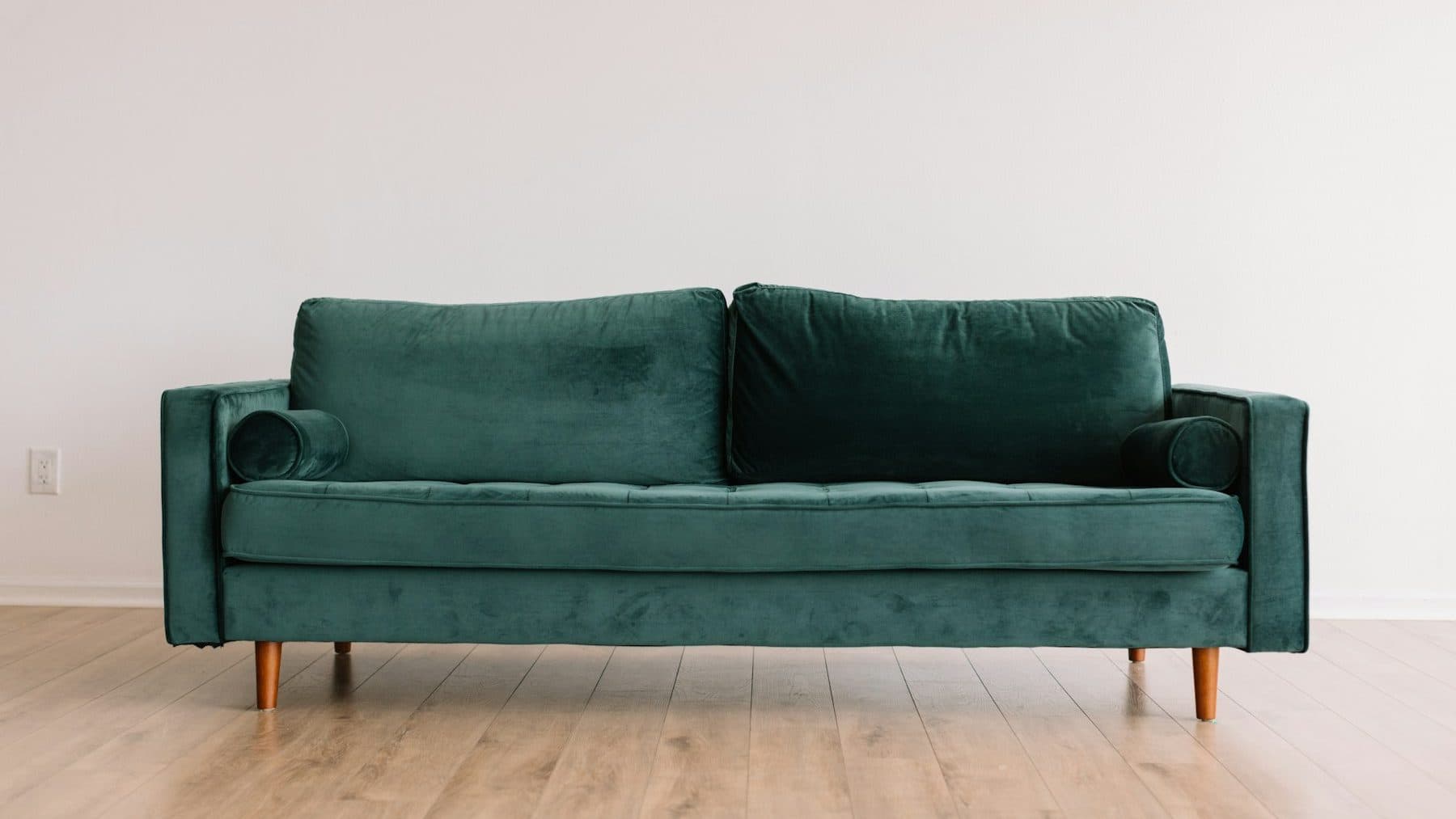 A green velvet three-seater sofa on a pale wooden floor