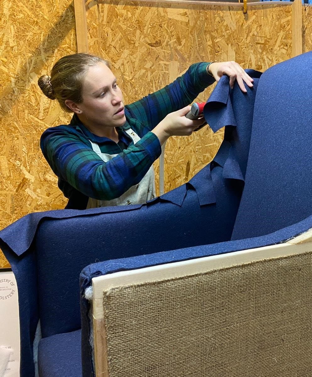 Gemma Broad, co-founder of We Are Repairs, fitting blue wool to the arm of a chair in her workshop